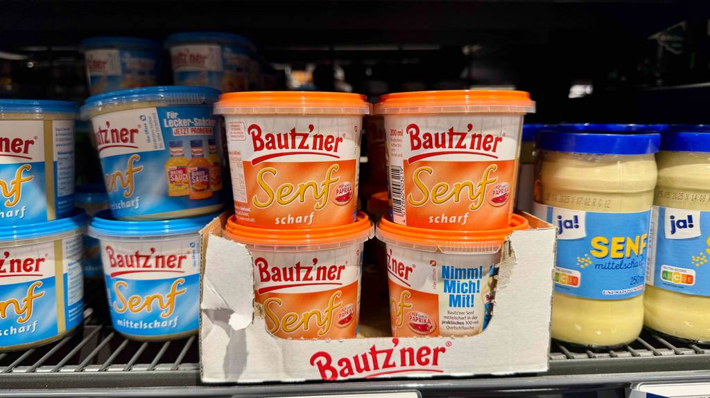 Mehrere Packungen des getesteten scharfen Senfs stehen in einem Regal neben mittelscharfem Senf.