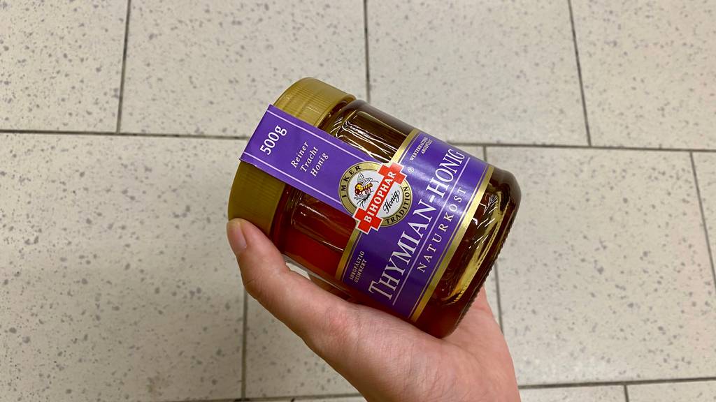 Thymianhonig im Test: Eine Hand hält ein Glas vor hellen Hintergrund