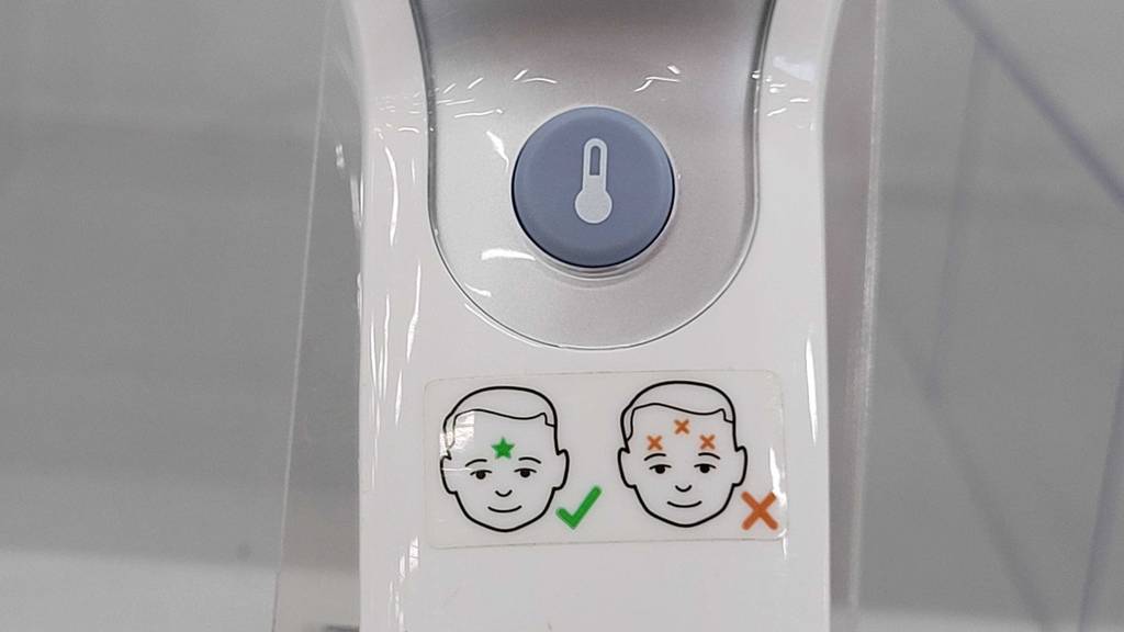Test: Der Knopf und die Applikation, wie man den Stirnthermometer verwendet im Fokus.
