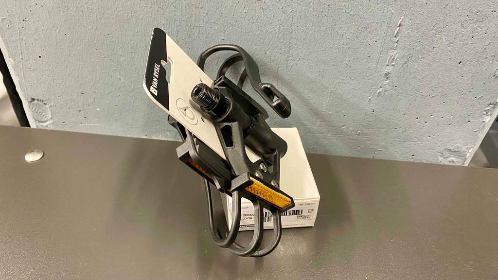 Ein getestetes Rennrad-Pedal von der Seite vor einer grauen Wand.