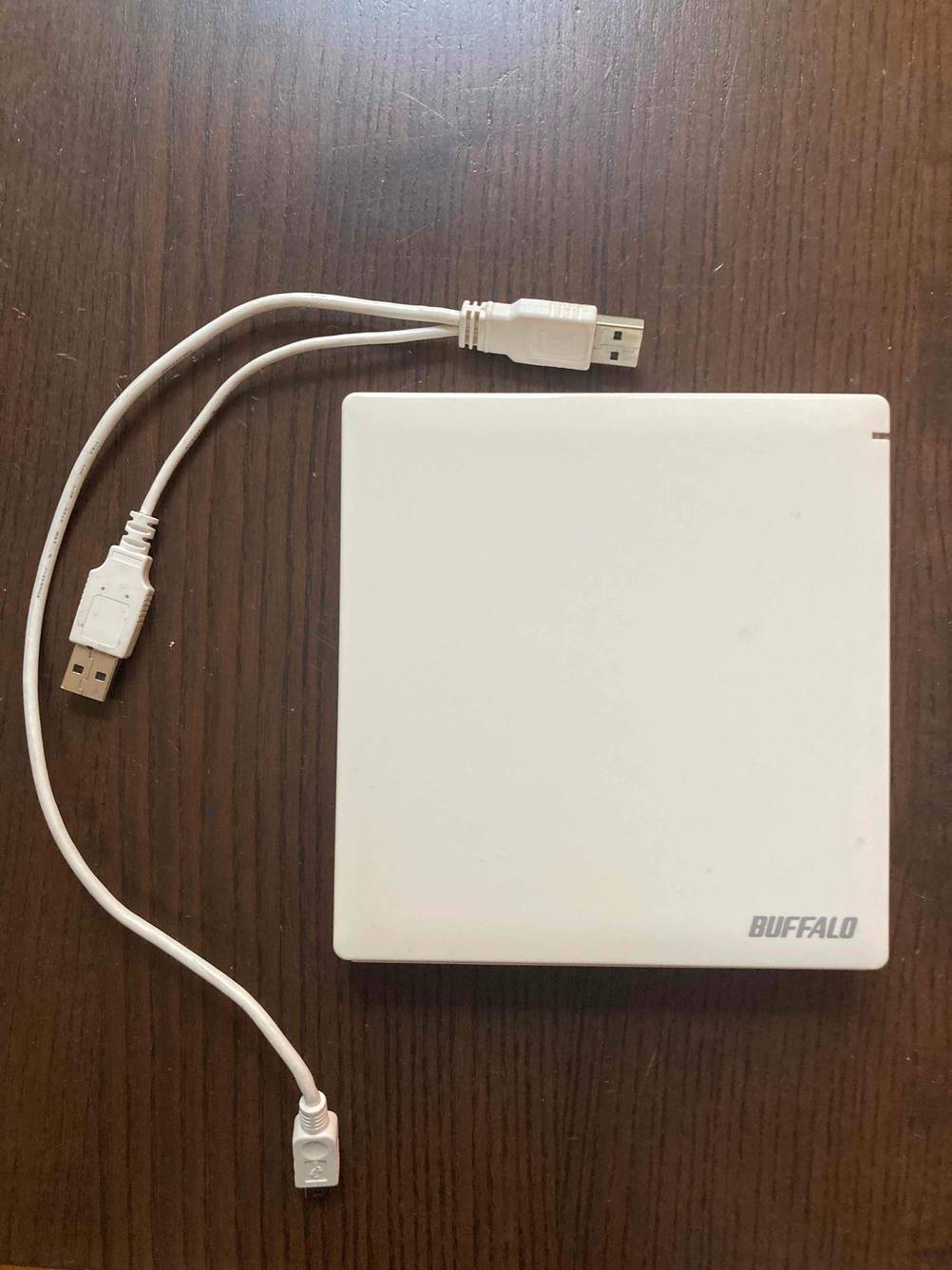 Ein getestetes Externes DVD-Laufwerk auf einer Holzfläche, Kabel liegen daneben.