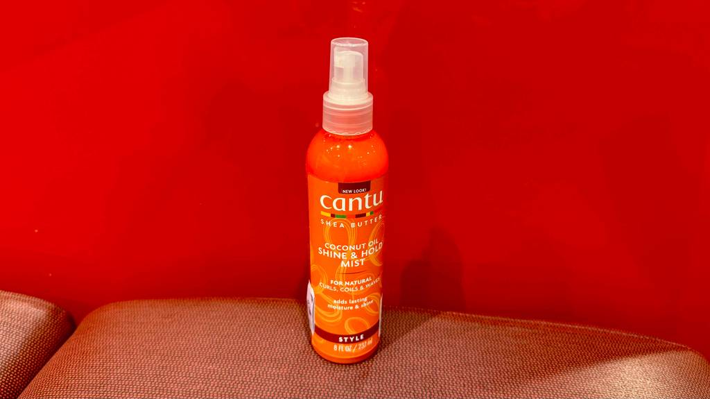 Der getestete Lockenspray von Cantu steht vor einer roten Wand.