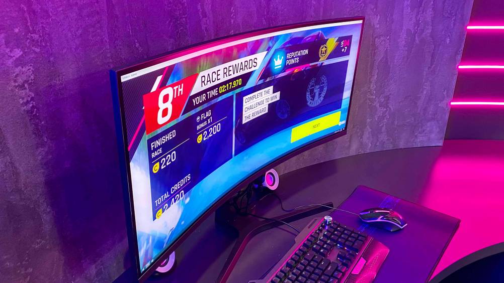 Ein getesteter Curved-Gaming-Monitor von der Seite auf einer dunklen Fläche mit Maus und Tastatur.