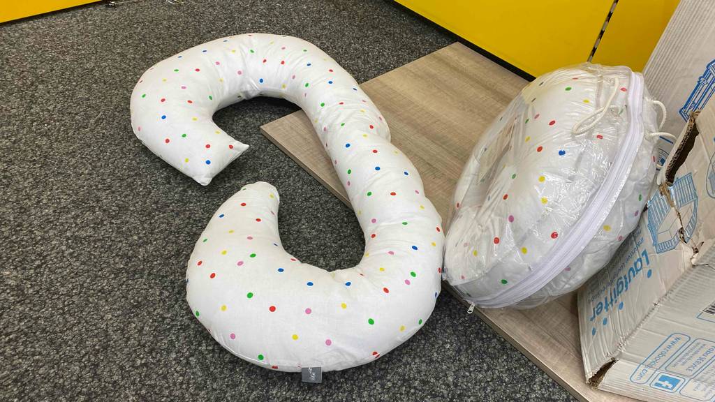 Im Test: Zwei Schwangerschaftskissen, eins verpackt, eines aufgerollt liegen auf einem dunklen Untergrund.