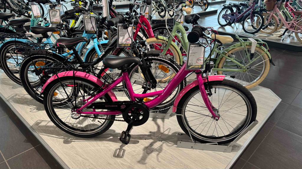 Mädchenfahrrad 20 Zoll im Test: Gesamtansicht des pinkfarbenen Modells, das vor anderen Fahrrädern auf einem Podest im Geschäft steht.