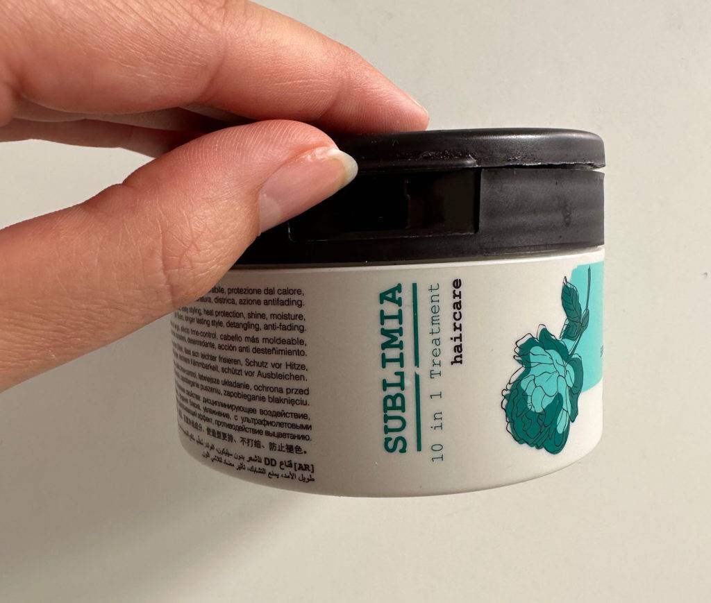 Haarmaske getestet: eine Haarmaske mit schwarzem Verschluss wird vor einer weißen Wand gehalten.