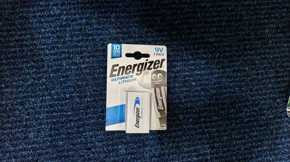 Die getestete 9V-Lithium-Batterie, die sich in der Verpackung befindet, liegt auf einem blauen Stoff.