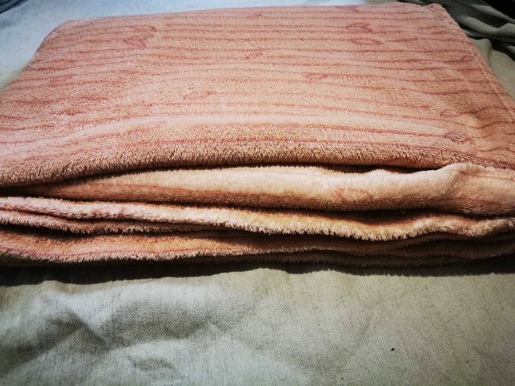Die rosa Fleecedecke im Test liegt zusammengefaltet auf einer Matratze.