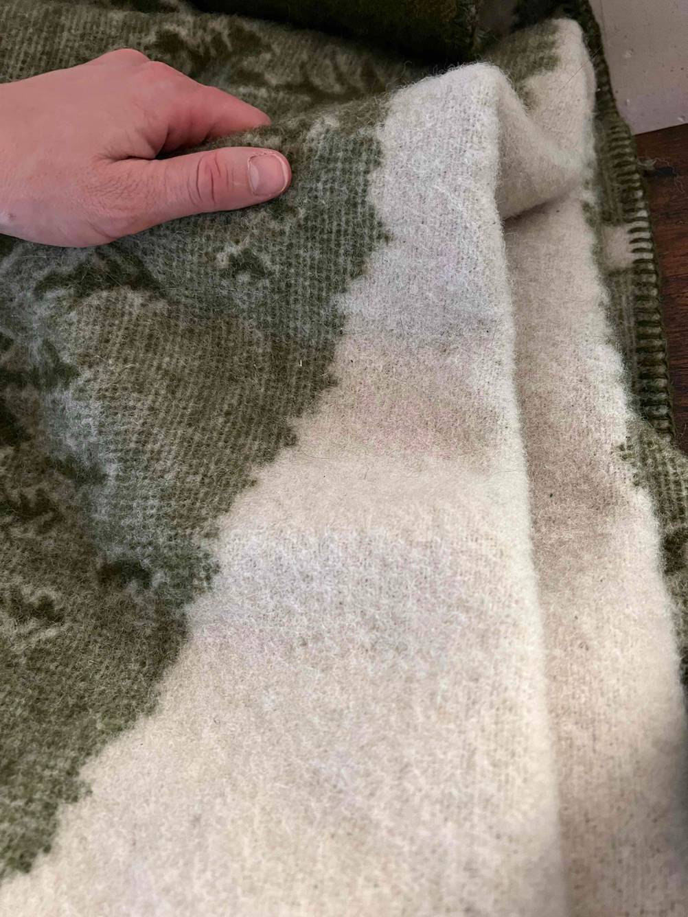 Eine Hand hält eine getestete Baumwolldecke leicht hoch.