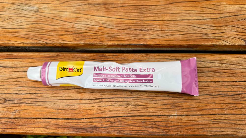 Eine Tube Malzpaste für Katzen, die getestet wurde, liegt auf einem Untergrund aus Holz.