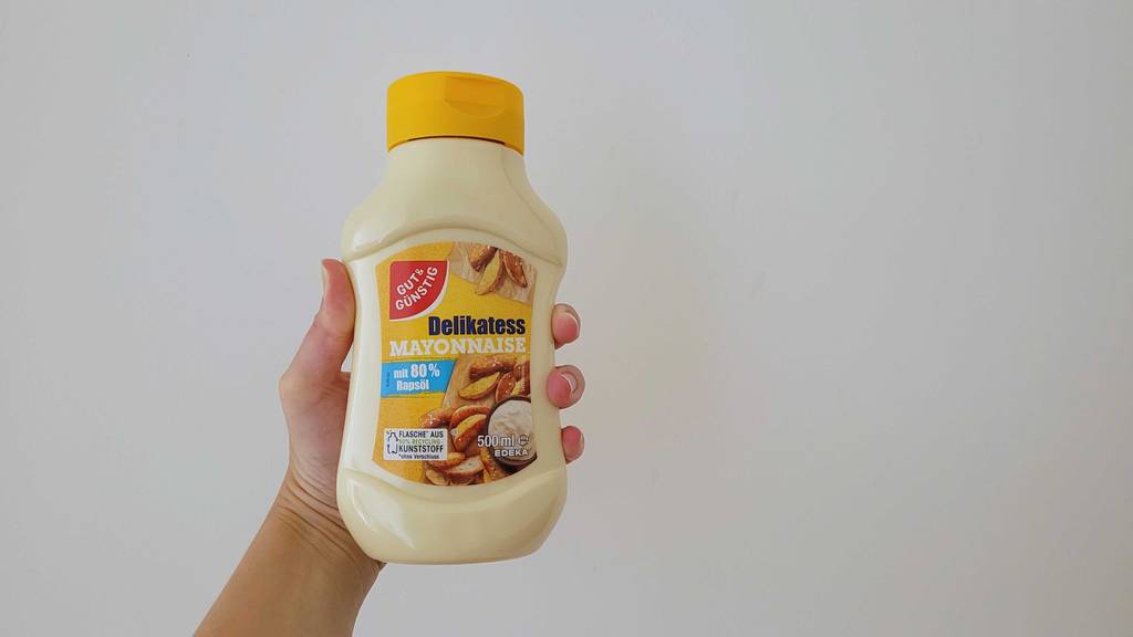 Mayonnaise im Test: Eine Hand hält eine Flasche vor eine helle Oberfläche