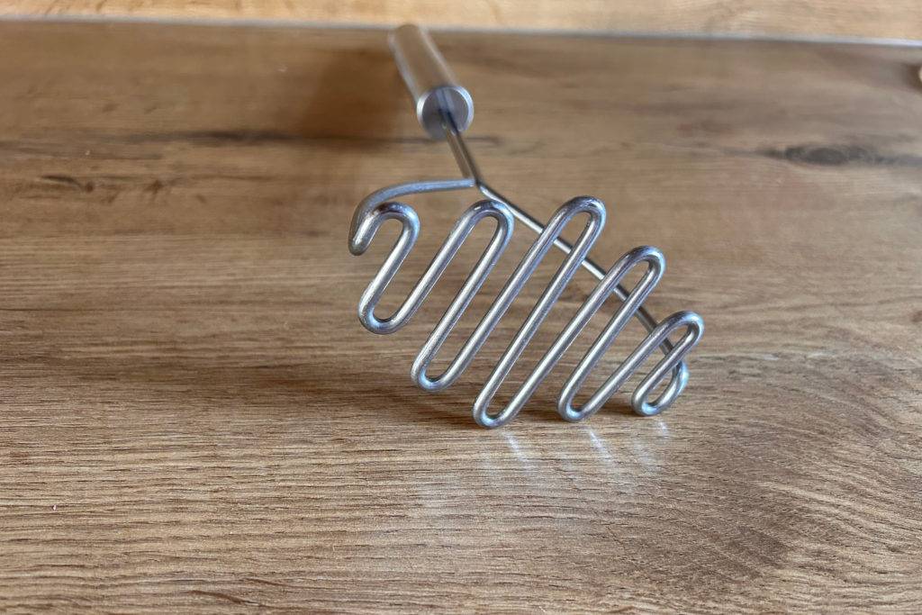 Vorderer Teil von Kartoffelstampfer auf einer Holzoberfläche.