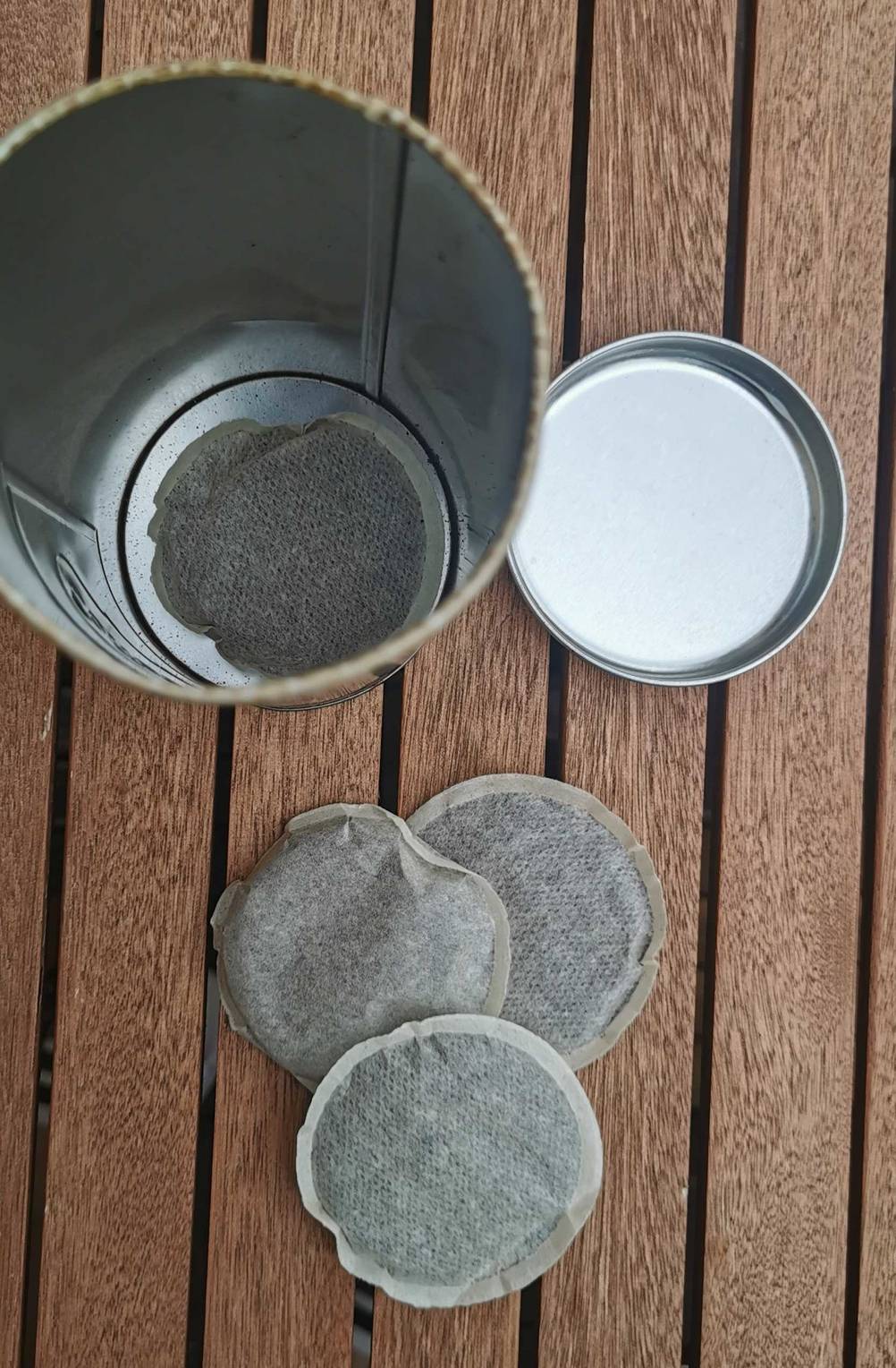 Drei Kaffeepads auf einem Tisch und geöffnete Dose daneben.