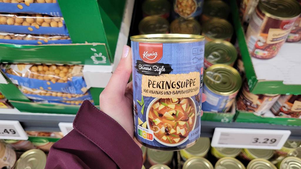 Eine getestete Dose Asia-Suppe wird in der Hand vor einem Regal gehalten.