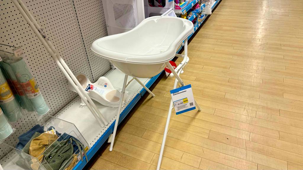 Babybadewanne mit Gestell im Test: eine Babybadewanne steht vor einem Regal mit Etikett darauf ersichtlich.