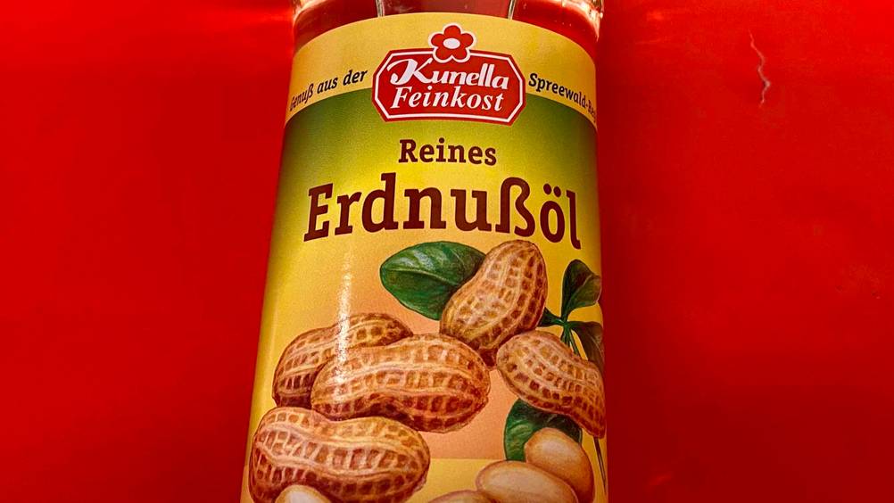 Erdnussöl im Test: Flasche in Nahaufnahme auf rotem Untergrund