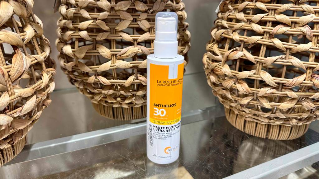 Eine La-Roche-Posay-Sonnencreme im Test steht in der Sprühflasche aus Kunststoff vor drei Korblampen.