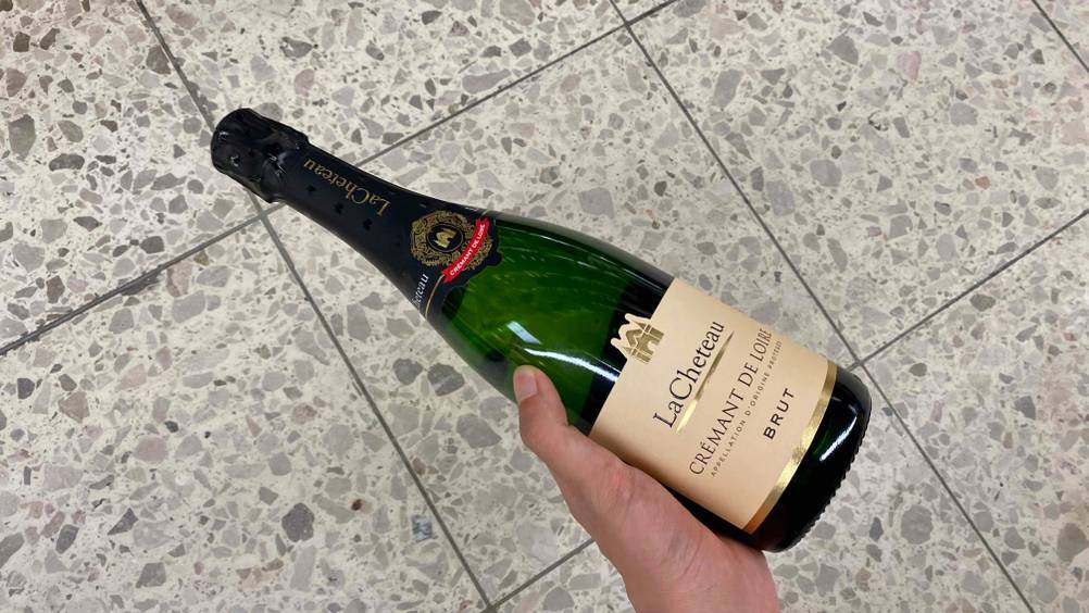 Crémant de Loire im Test: Eine Hand hält eine Flasche vor einen hellen Fließenboden