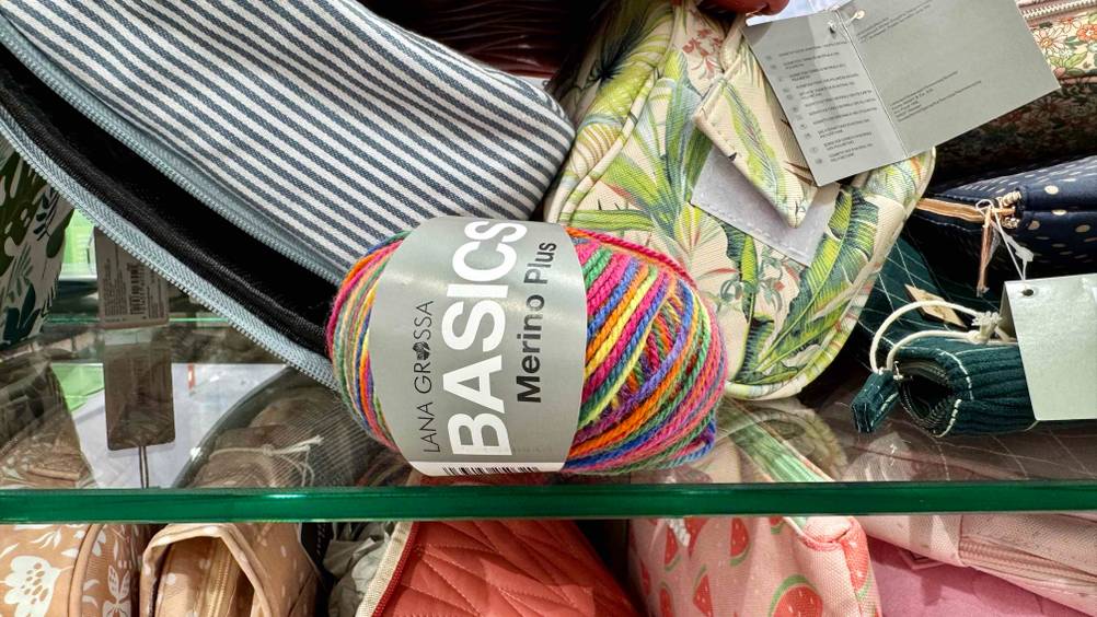 Die getestete Regenbogen-Wolle liegt in einem Regal, worin sich Kosmetiktaschen befinden.