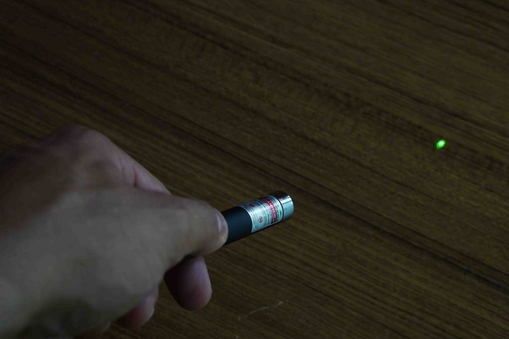 Laserpointer-Test: Laserpointer wird betätigt - Grüner Punkt auf Holzfläche ersichtlich.