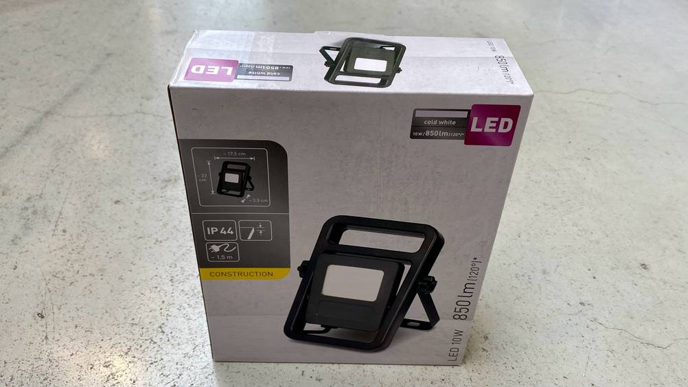 Auf einem hellen Boden steht ein getesteter LED-Baustrahler in seiner Verpackung.