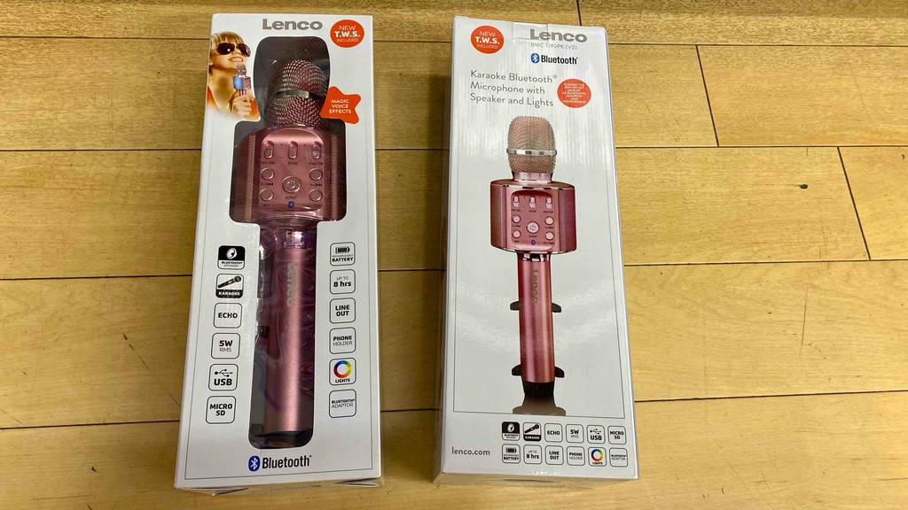 Auf einem Holzboden liegen zwei getestete Karaoke-Mikrofone in ihrer Originalverpackung.