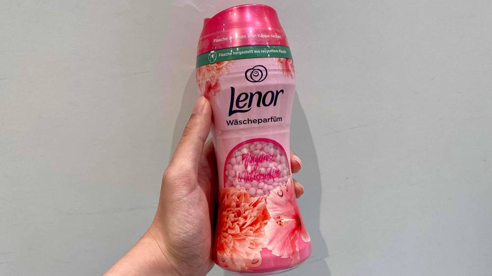 Eine Hand hält eine Flasche des getesteten Wäscheparfüms vor eine hellen Wand.