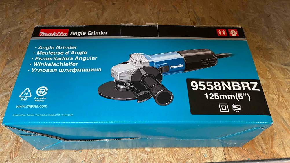 Ein getesteter Makita-Winkelschleifer 125 in seiner Originalverpackung liegt auf einer Holzfläche.