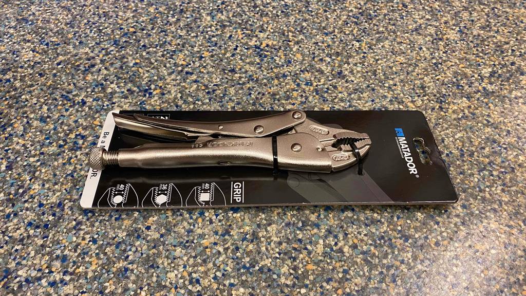 Die getestete Gripzange in ihrer Originalverpackung horizontal auf einer bunten Unterlage
