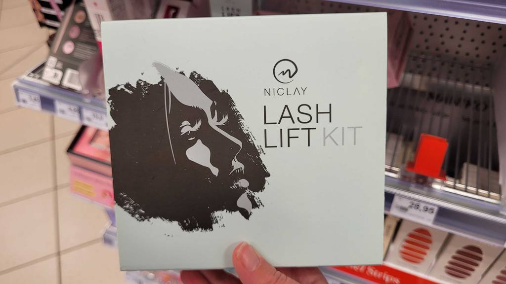 Wimpernlifting-Set im Test: Die Packung wird in der Hand vor einem Regal gehalten.