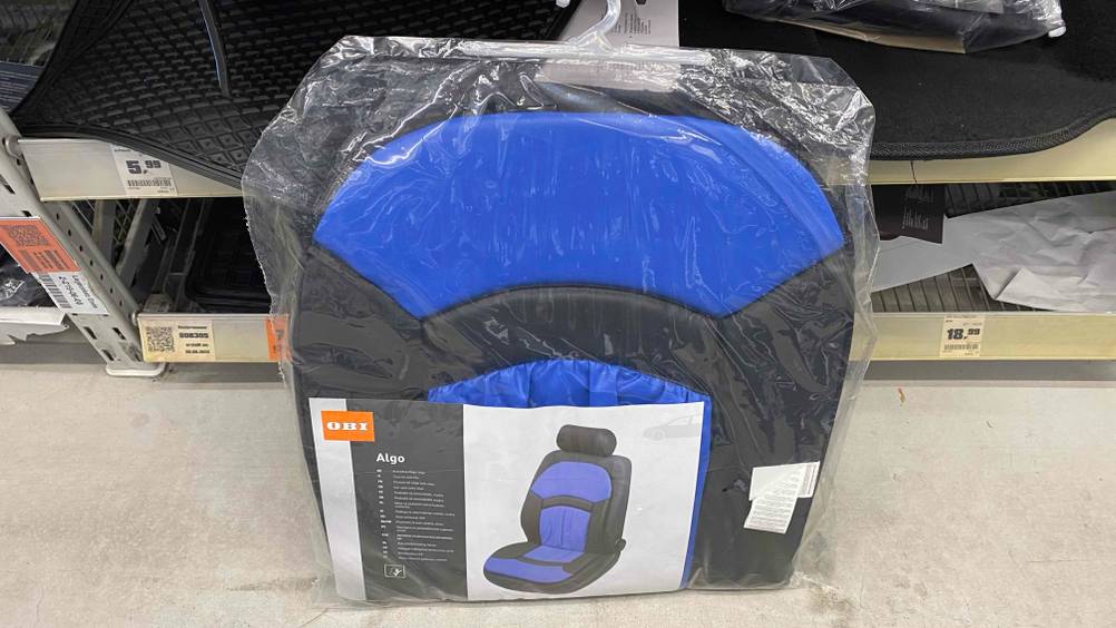 Eine getestete Autositzauflage in ihrer Verpackung steht auf einer hellen Oberfläche vor einem Regal.
