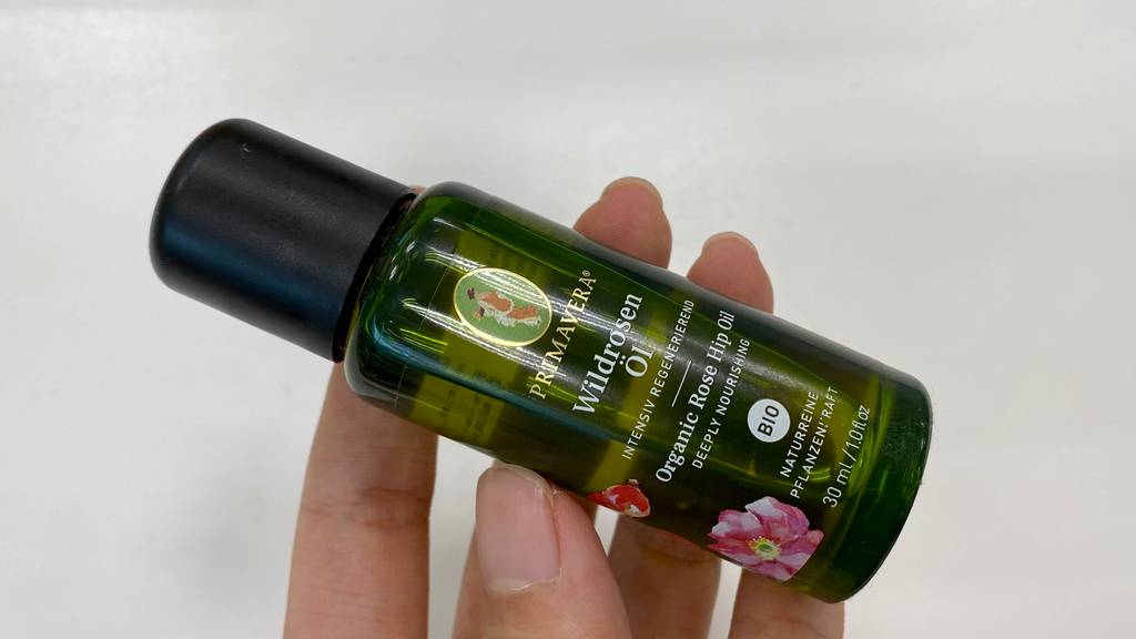 Rosenöl-Test: grün gefärbte Flasche in der Hand vor weißer Wand.