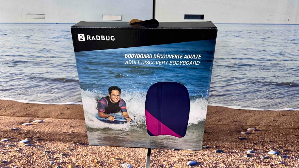 Das getestete aufblasbares Bodyboard steht vor einem Aufsteller im Design eines Strandes.