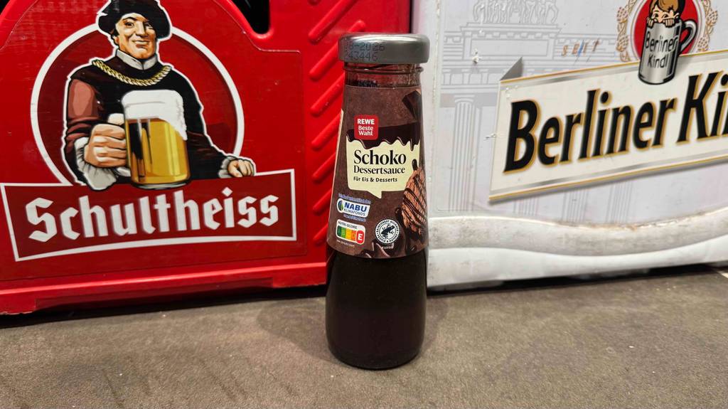 Eine Flasche der getesteten Schokoladensauce steht vor Bierkisten.