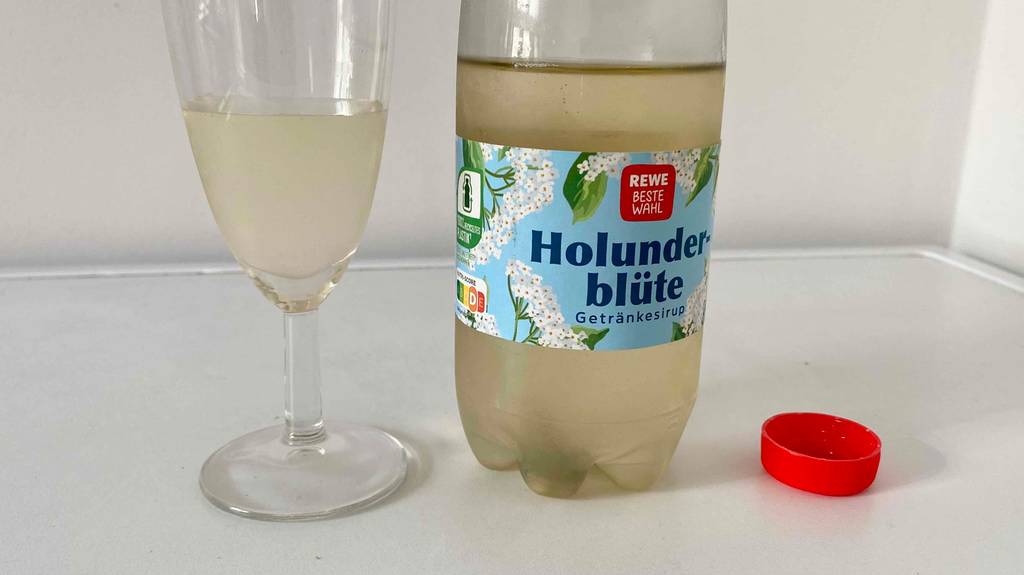 Flasche von getestetem Holunderblütensirup und daneben Glas mit Saft zu sehen.