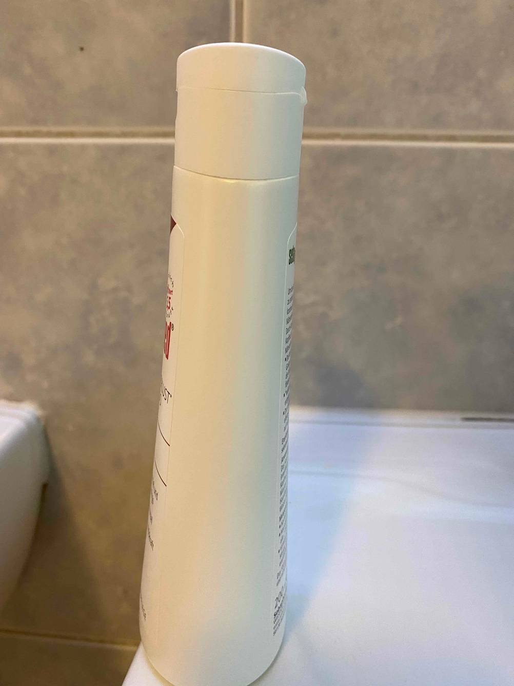Eine Flasche getestetes Shampoo gegen Haarausfall steht seitlich auf einem Waschbecken.