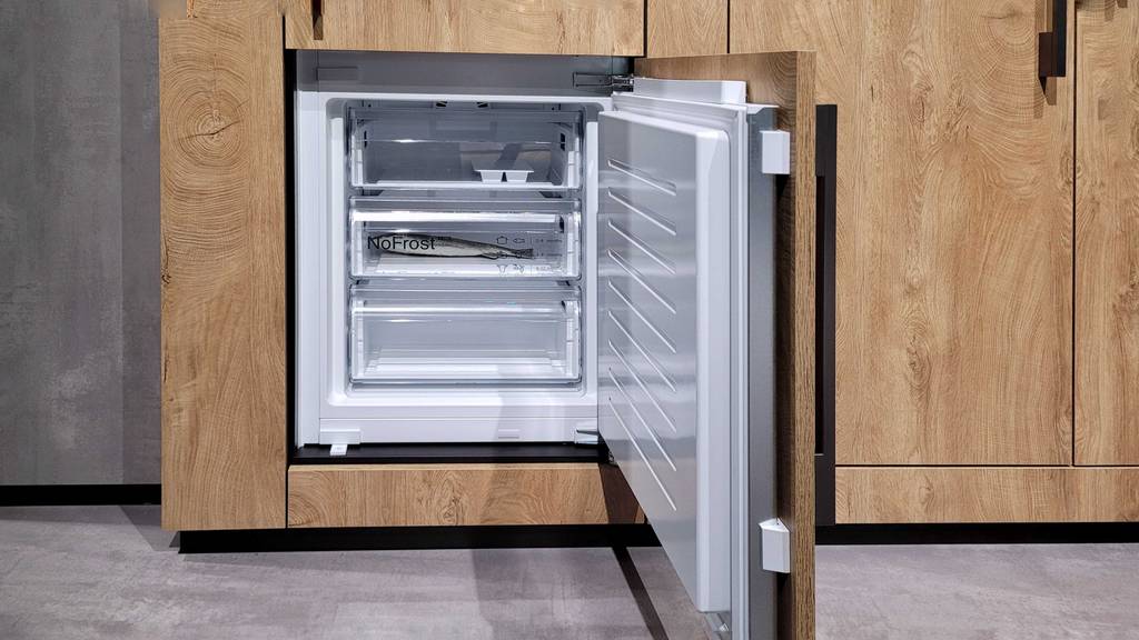 Einbau-Kühl-Gefrierkombination im Test: stehend, offene Fronttür des unteren Gefrierfaches, Innenraumansicht, diverse Schubläden, in Küchenzeile mit Holzoptik.