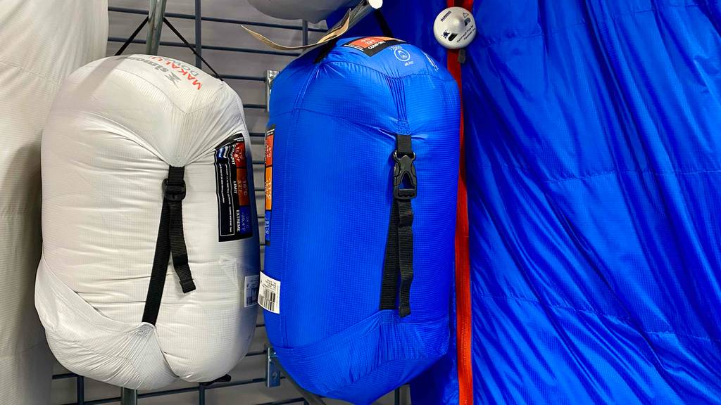 Daunenschlafsack getestet: eine weiße und blaue Aufbewahrungstasche mit Daunenschlafsäcken darin in einem Regal hängend.