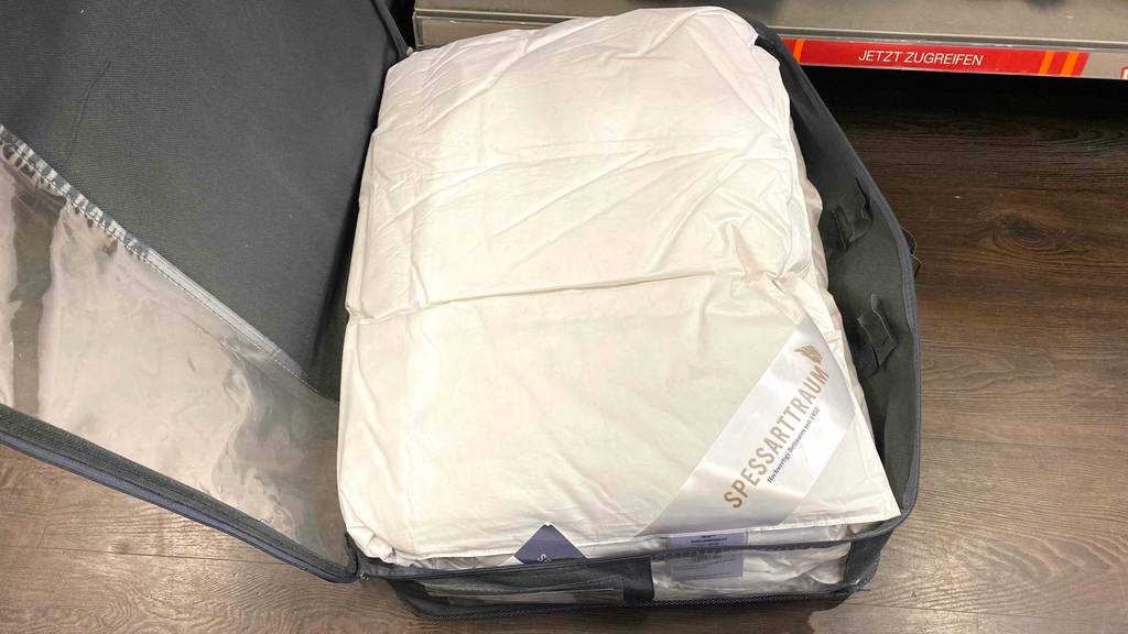 Daunendecke-155x220-Test: eine zusammengefaltete Daunendecke in einer geöffneten Tragetasche, die mit einem Reißverschluss verschlossen wird.
