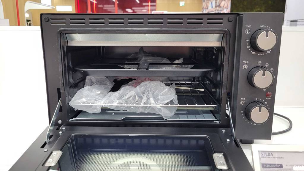 Ein geöffneter, getesteter Minibackofen mit Drehspieß steht in einem Geschäft.