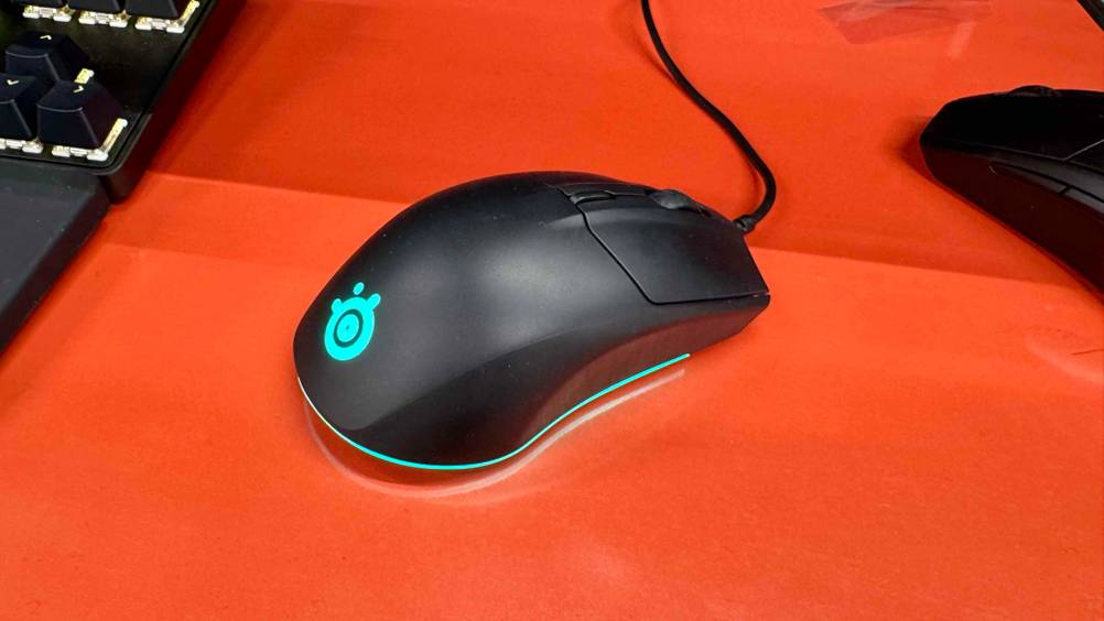 Die beleuchtete SteelSeries-Maus, die getestet wurde ist auf einer roten Oberfläche platziert.