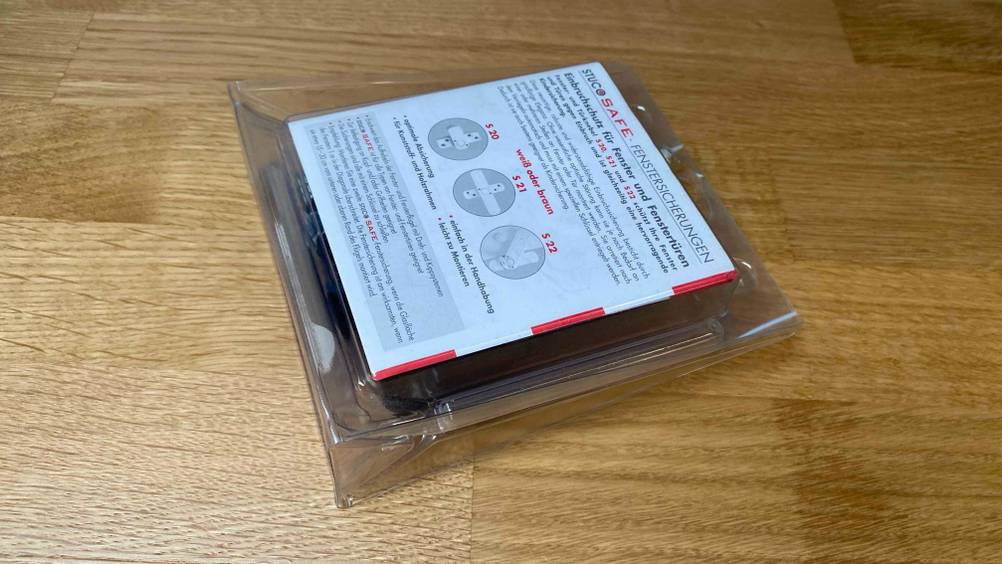 Eine getestetee Fenstersicherung verpackt auf einem Holzboden liegend.