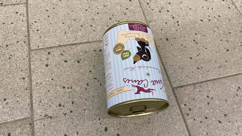 Auf einem hellen Fließenboden liegt umgedreht eine Dose Welpen-Nassfutter