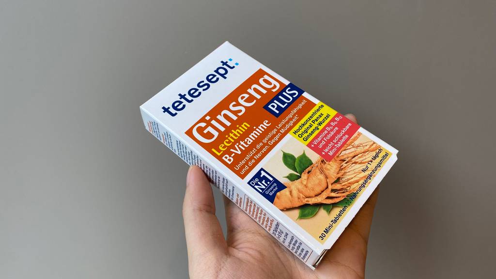 Ginseng-Kapseln im Test: Eine Hand hält eine Packung Kapseln gegen einen grauen Hintergrund