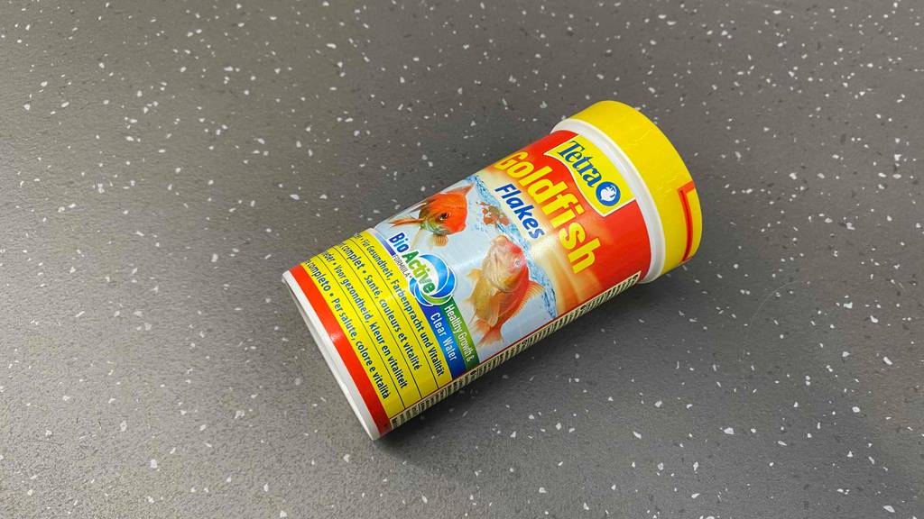 Goldfischfutter-Test: gelbe Dose Goldfischfutter in Form von Flakes auf einem Boden liegend.