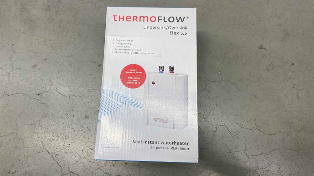 Im Test: Ein verpackter ThermoFlow Mini-Durchlauferhitzer liegt auf einem grauen Boden.