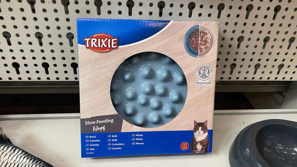 Ein getesteter Anti-Schling-Napf für Katzen steht vor einem Lochgitter auf einer hellen Oberfläche.