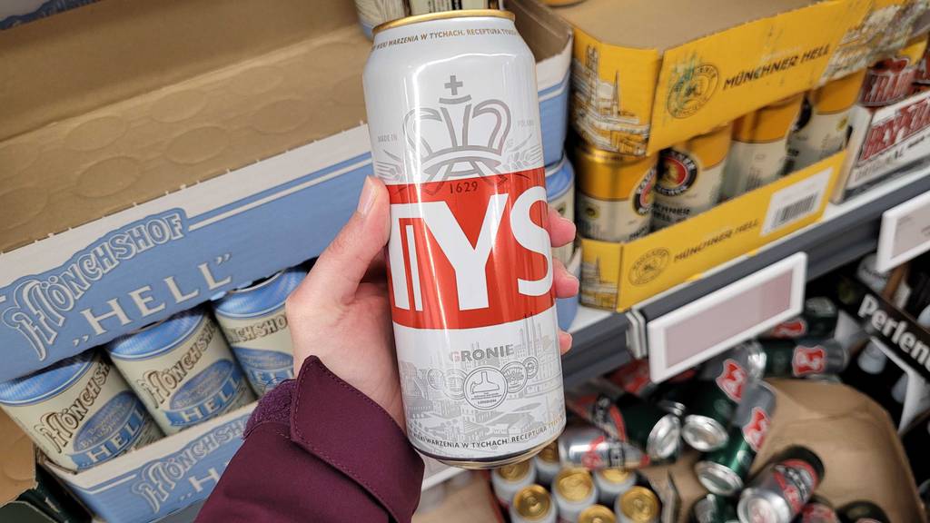 Eine getestete Dose polnisches Bier wird in der Hand vor einem Regal gehalten.