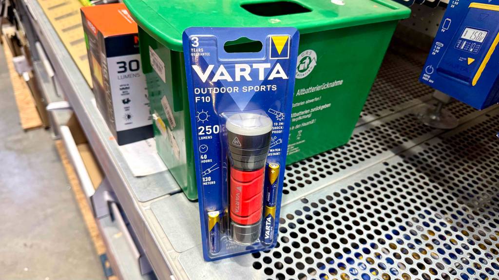 Die getestete Varta-Taschenlampe mit dem roten Handgriff befindet sich in der Verpackung auf einem Verkaufsregal.