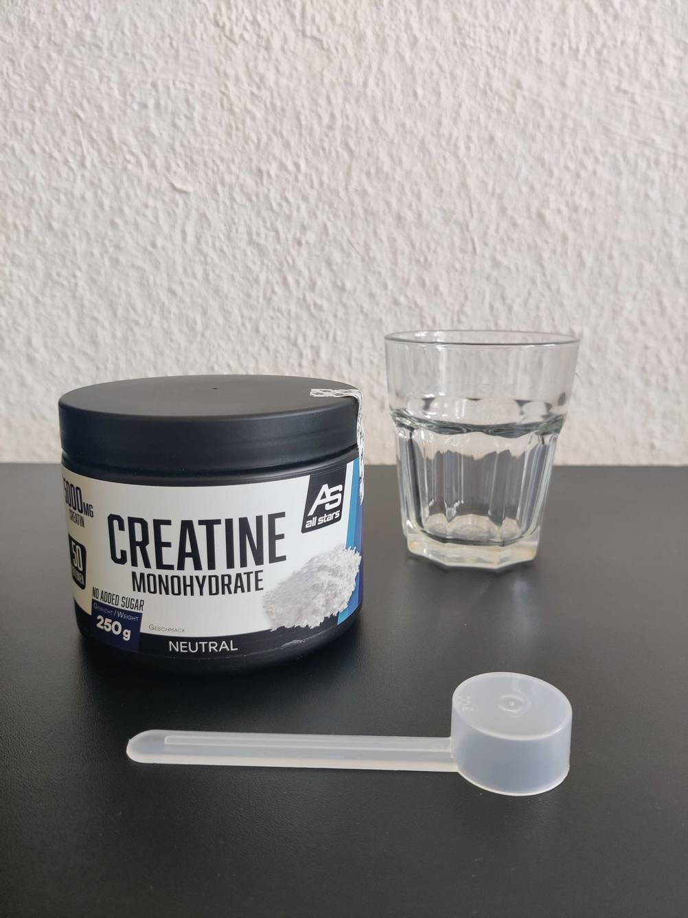Creatinpulver mit Löffel davor und Glas daneben.